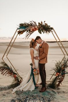 a newly married couple kissing in front of an arch made out of plants and branches