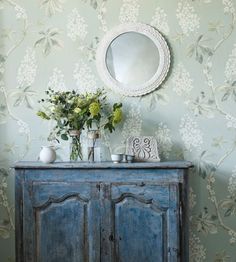 a blue cabinet with flowers and vases on it in front of a wallpapered background