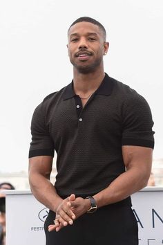 a man standing in front of a crowd wearing a polo shirt and black pants with his hands together