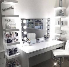 a white desk topped with lots of drawers and lights next to a chair in front of a mirror