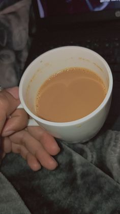 a person holding a cup of coffee in front of a laptop