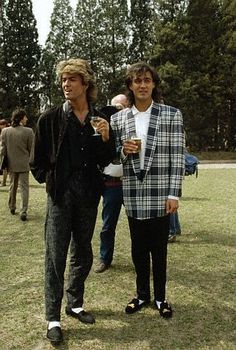 two men standing next to each other on a field with trees in the back ground