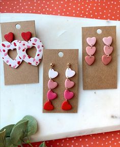 three pairs of heart shaped earrings are displayed on a table next to some paper hearts