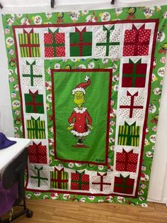 a green christmas quilt with the grin on it's back and presents all around