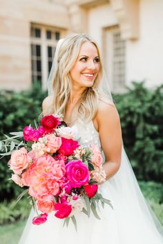 a woman in a wedding dress holding a bouquet of pink and red flowers with greenery behind her