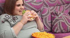 a pregnant woman sitting on a couch eating a hamburger and french fries