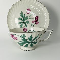 a tea cup and saucer with flowers painted on the side, sitting next to each other