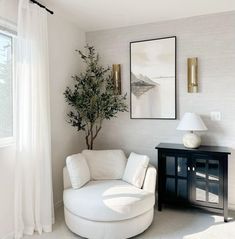 a living room with white furniture and a tree in the corner on the side table