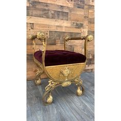 a gold chair with a red velvet cushion on it's back and legs, in front of a wooden wall