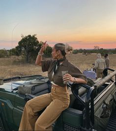 a woman sitting on the back of a green truck in front of an open field