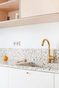 a kitchen with white cabinets and gold faucet, marble counter tops and wooden shelves