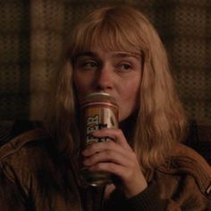 a woman with long blonde hair drinking from a can in front of her face and looking at the camera