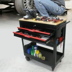 a man working on a workbench in front of a car with tools and other items