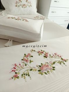 a white bed with pink flowers on it next to a pillow case and two pillows