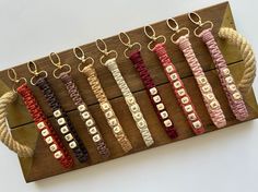 several different colored bracelets hanging on a wooden board with metal hooks and cords attached to them