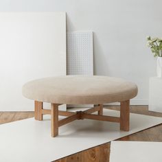 a round ottoman sitting on top of a wooden floor next to a vase with flowers