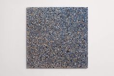 an abstract painting with blue and gold speckles on the ground in front of a white wall