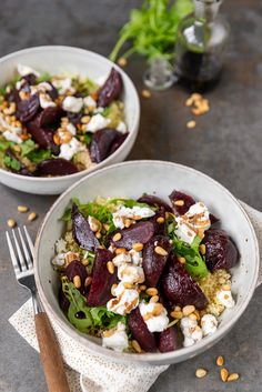 two white bowls filled with beets, feta cheese and nuts on top of a table