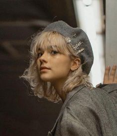 a woman with blonde hair wearing a gray hat and jacket looking off into the distance