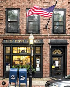 an american flag flying in front of a post office with two lawn chairs on the sidewalk