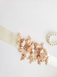 a bridal sash with flowers and pearls on the side, next to a pearl bracelet