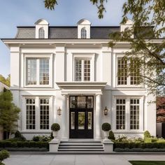 a large white house with black doors and windows on the front door is surrounded by greenery