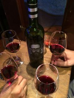 two people are holding wine glasses with red wine in front of them on a wooden table