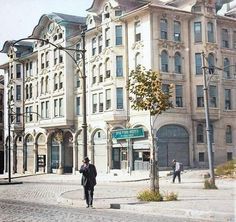 a man walking down the street in front of a large building with many windows on it