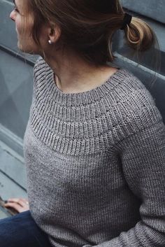 a woman sitting on the ground with her hair in a ponytail wearing a gray sweater