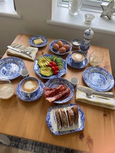 a wooden table topped with blue and white plates filled with food next to a window