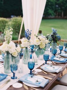 the table is set with blue and white plates, silverware, and vases