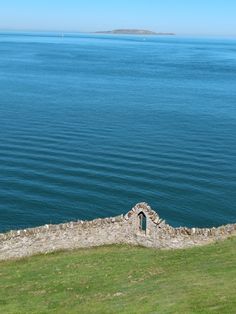 an old stone building sitting on top of a lush green hillside next to the ocean