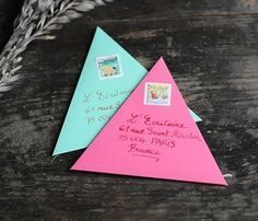 two pink and blue envelopes sitting next to each other on top of a wooden table