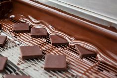 chocolate is being made on a conveyor belt with melted chocolate squares in the foreground