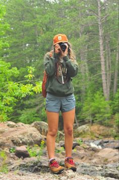 a woman standing on top of a rock next to a forest filled with lots of trees