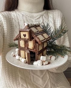 a woman holding a white plate with a small house on it and marshmallows