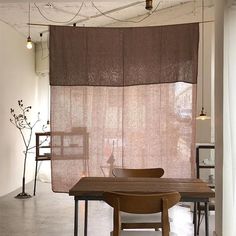 a table and chairs are sitting in front of a window with curtains hanging from the ceiling