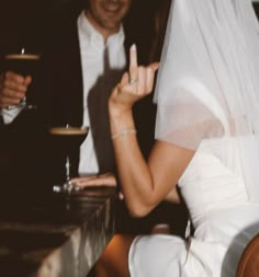 a bride and groom sitting at a table with their hands in the air as they hold wine glasses