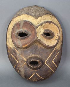 an african mask with two holes in the middle and one hole at the bottom, on a gray background