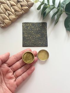 a person holding two small gold coins in their hand next to some other items on a table