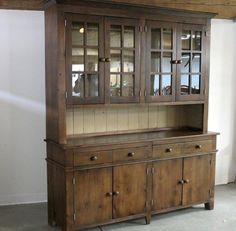 an old wooden china cabinet with glass doors on the top and bottom, in front of a white wall