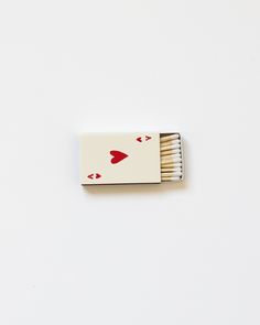 a matchbox with two matches in it on a white surface, one has red hearts and the other has an arrow