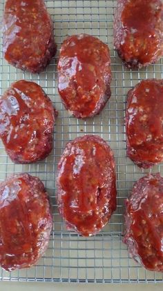 several hamburgers covered in ketchup sitting on a cooling rack