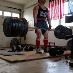 a man holding a barbell while standing in front of a gym equipment area with an american flag hanging on the wall