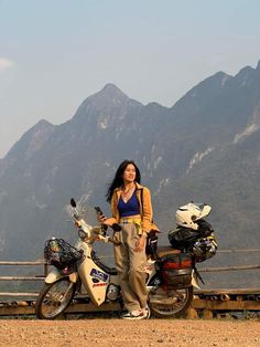 a woman standing next to a parked motor scooter in front of some mountains