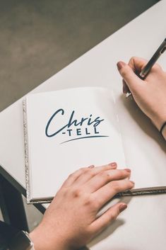 a person is writing on a book with a pen in their hand while sitting at a table