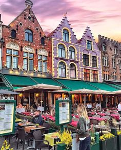 people are sitting at tables outside in front of some buildings with green awnings