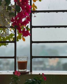 a glass filled with liquid sitting on top of a window sill next to flowers