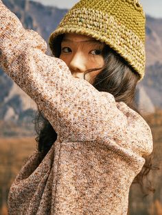 a young woman wearing a knitted hat and holding her arms up in the air