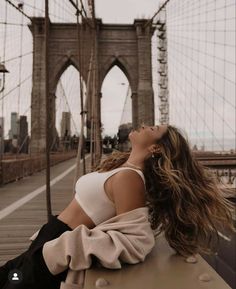 a woman sitting on a bench in front of the brooklyn bridge with her eyes closed